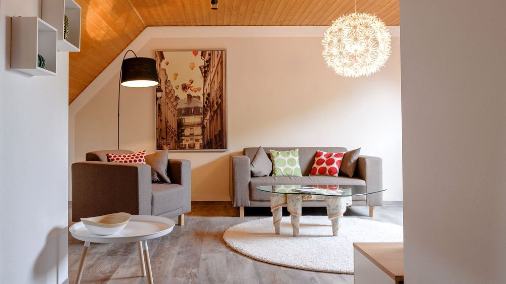 Wohnzimmer mit grauen Sofas, runder Lampe und großem Wandbild einer Stadtansicht.