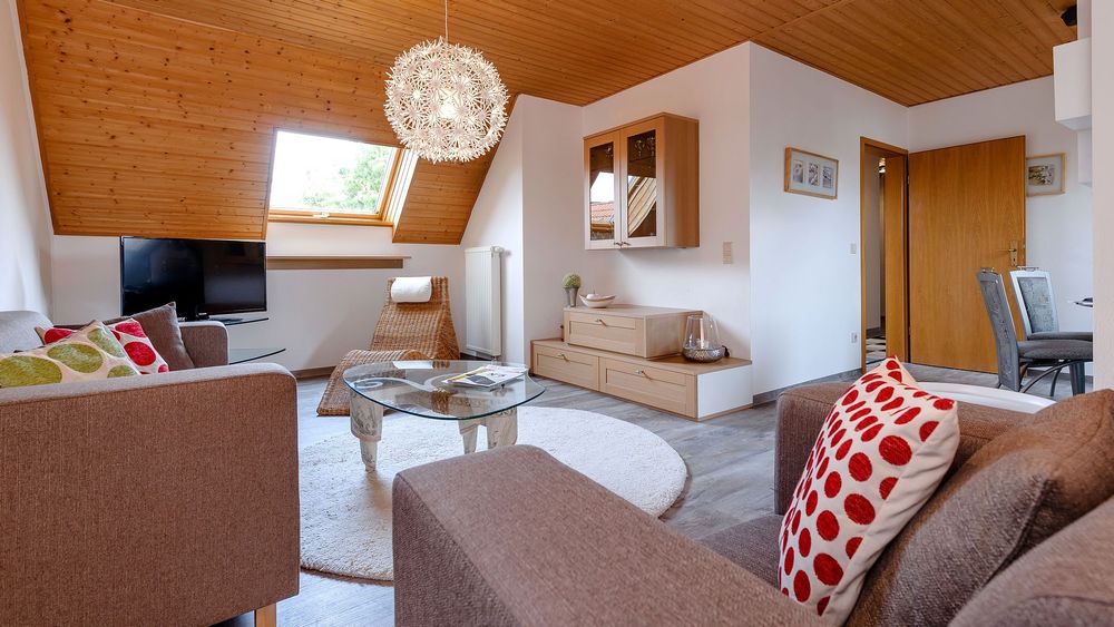 Wohnbereich mit Sofa, Glastisch und Holzdecke, Fernseher im Hintergrund.