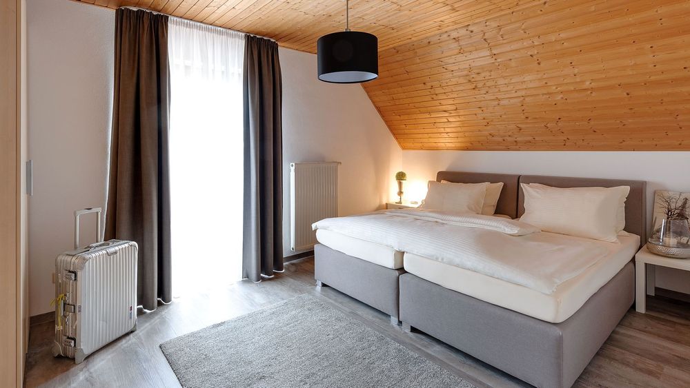 Helles Schlafzimmer mit Doppelbett, grauen Vorhängen und Holzdecke.