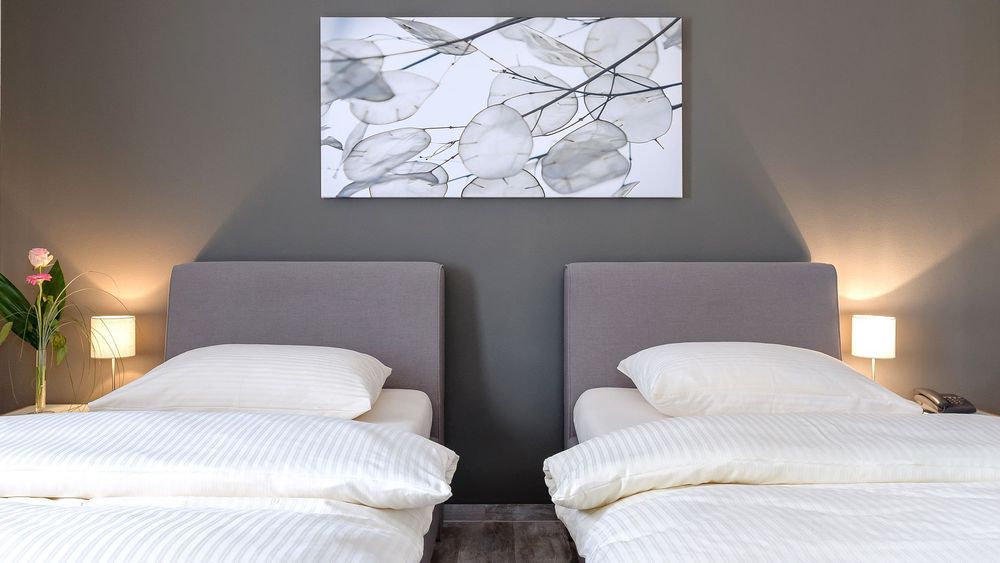 Zwei Einzelbetten mit grauen Kopfteilen und dunkler Wand, Bild mit Blättermotiv darüber.