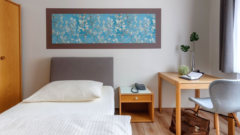 Kleiner Schreibtisch mit grauem Stuhl, Notizbuch und grüner Dekopflanze neben Fenster.